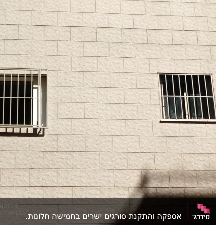 שני חלונות עם סורגים על קיר לבנים